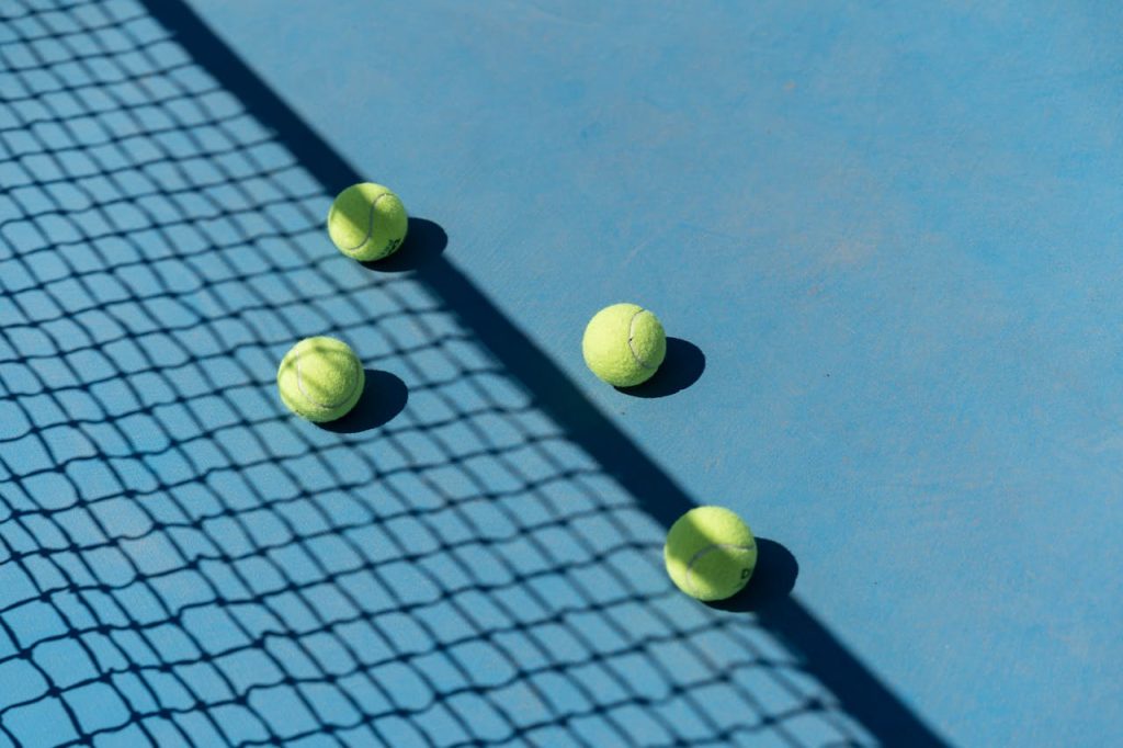 Four tennis balls resting on a blue tennis court with shadows from a net.
