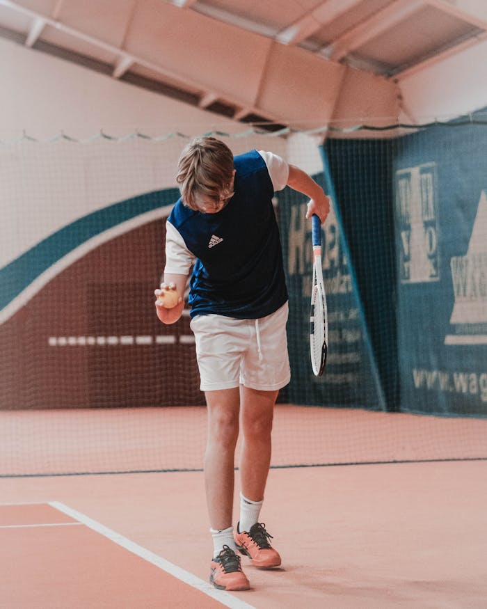 A young tennis player prepares to serve the ball on an indoor court, showcasing focus and technique.