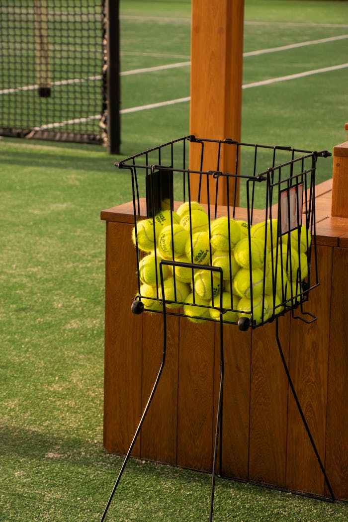 Basket filled with tennis balls on an outdoor tennis court, perfect for sports practice.