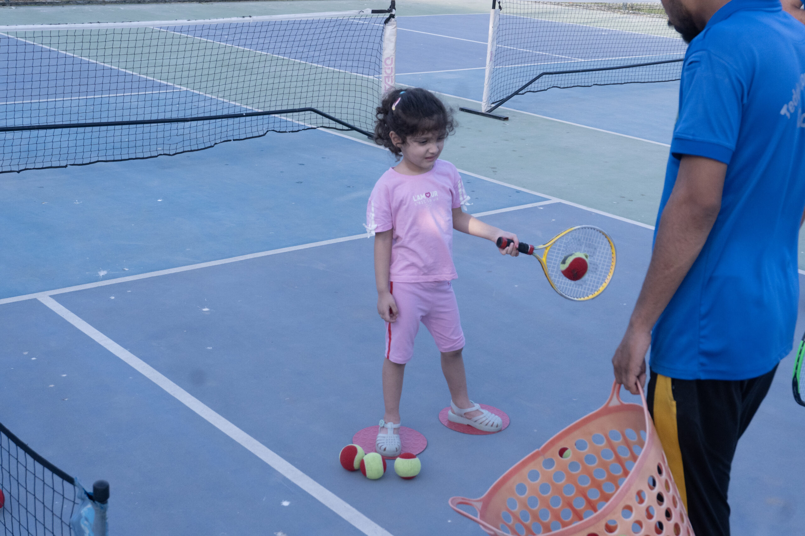 Young girl learning to hit a tennis ball with a coach during a kids holiday camp at Baseline Tennis Academy, DHA, Karachi