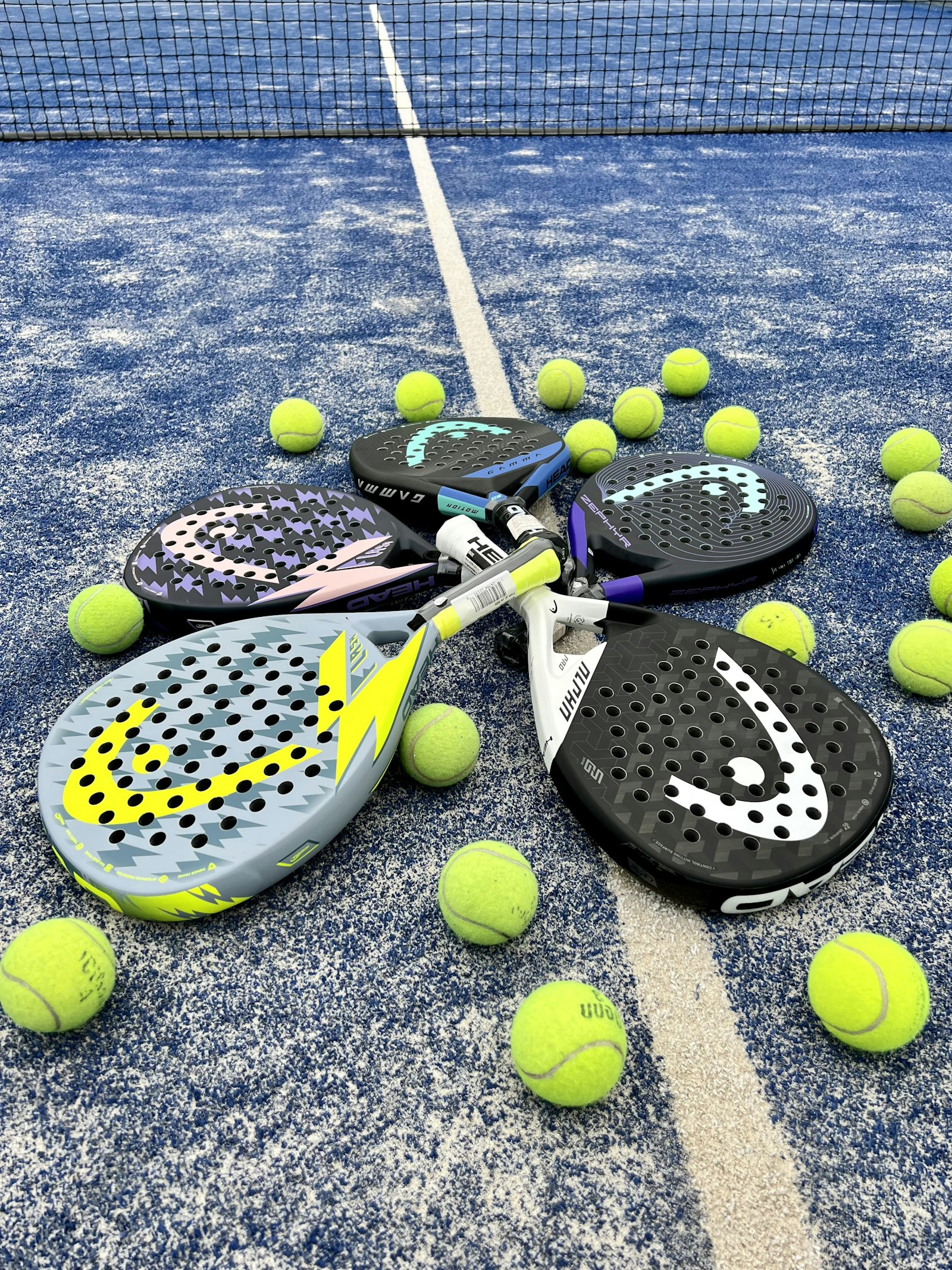 Four padel rackets and yellow balls laid out on a blue court, ready for a family doubles game at Baseline Tennis Academy in DHA, Karachi